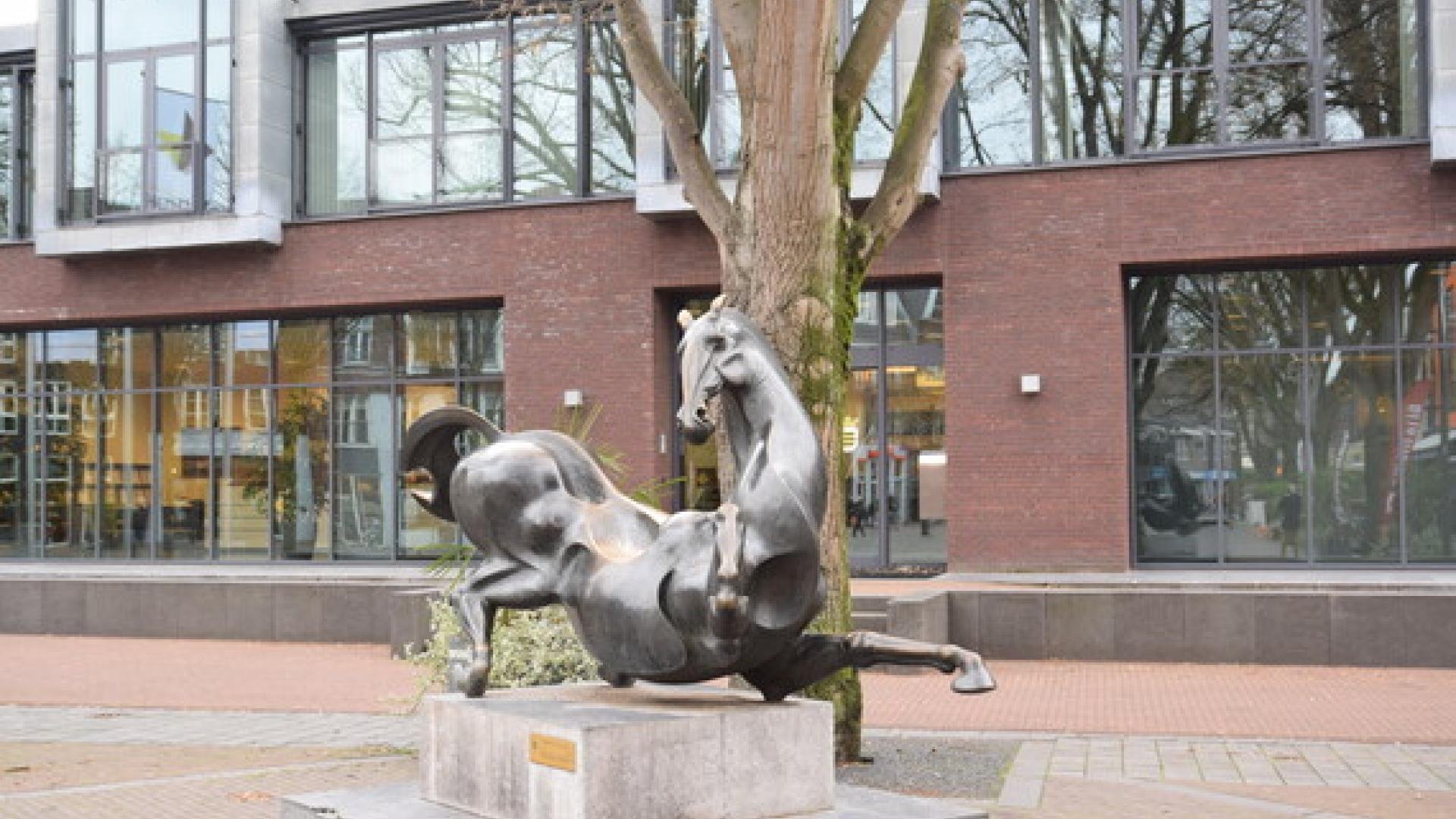 Entree gemeentehuis met op voorgrond een beeld van een dravend paard